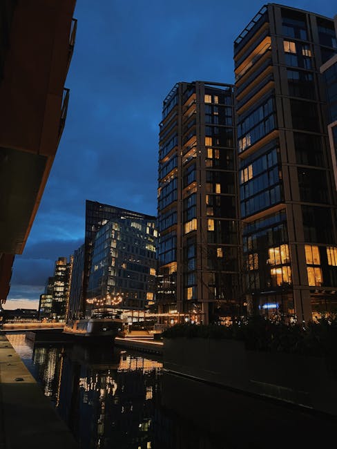 Exterior view of a modern residential building with a curved glass facade and multiple balconies, situated in an urban area. The building features a mix of materials, including glass, metal, and concr